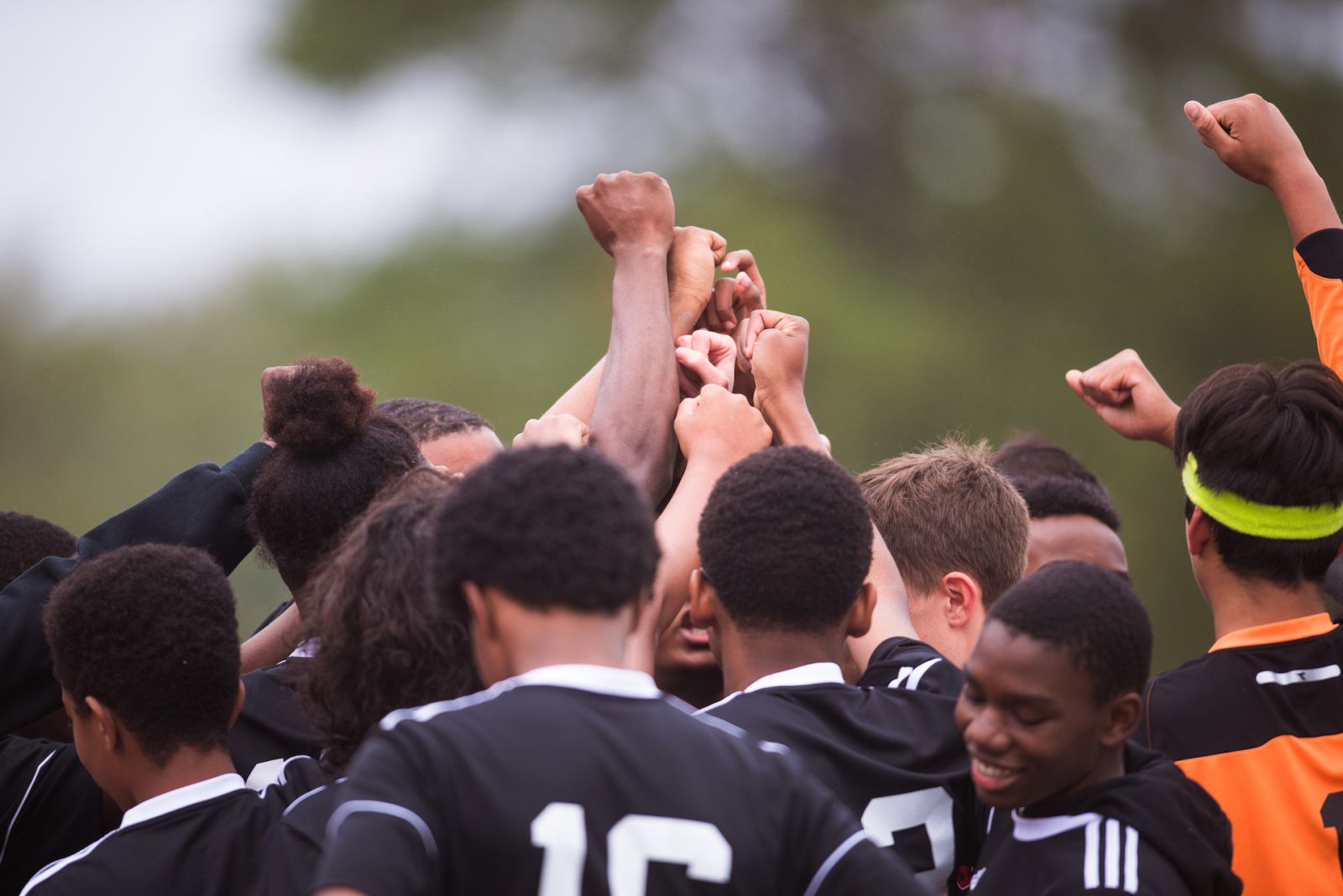 Photo of a boys' sports team in a huddle with their hands raised together