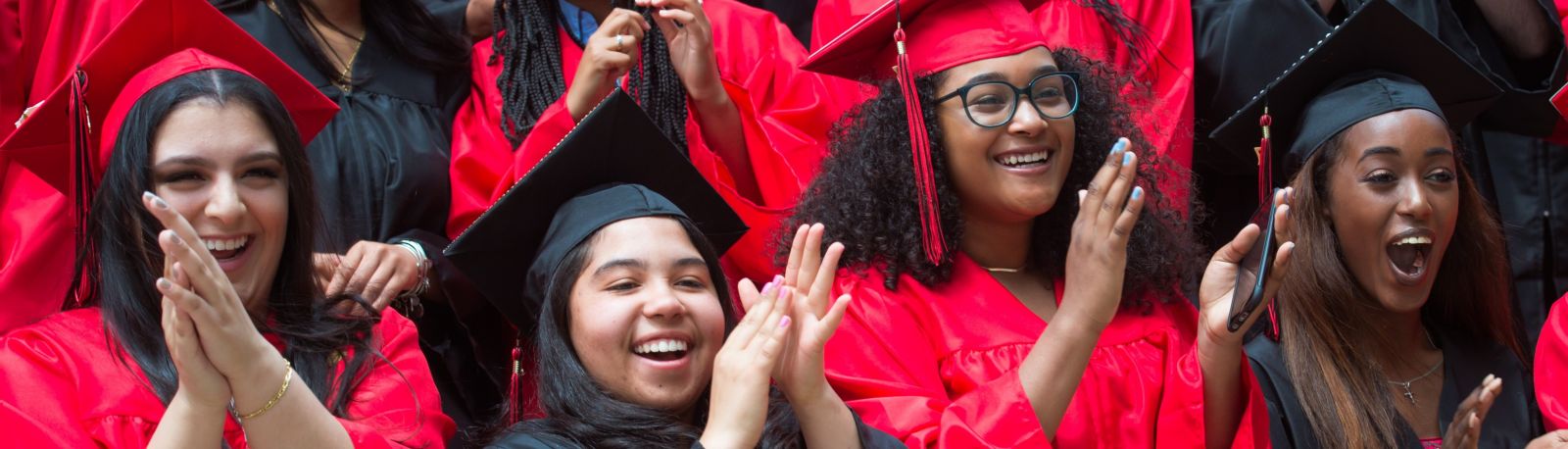 Photo of four students in graduation caps and gowns applauding