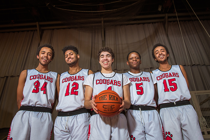 Photo of five boys basketball players in a group with the student in the middle holding a basketball
